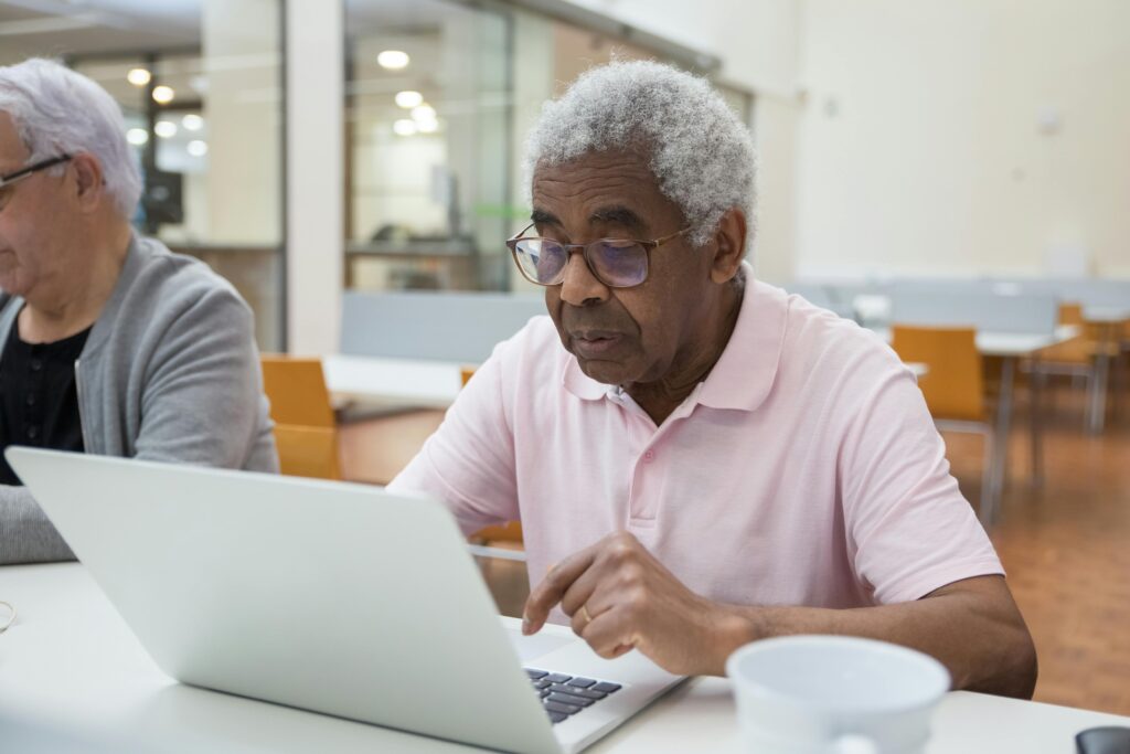Elderly men engage with laptops in a communal space, embracing technology and learning.